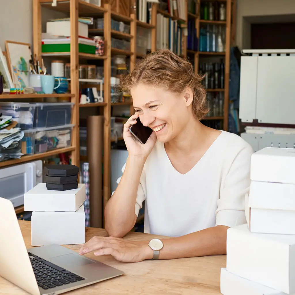 A small business owner with curly blond hair talks on the phone while scrolling a website for mental health tips